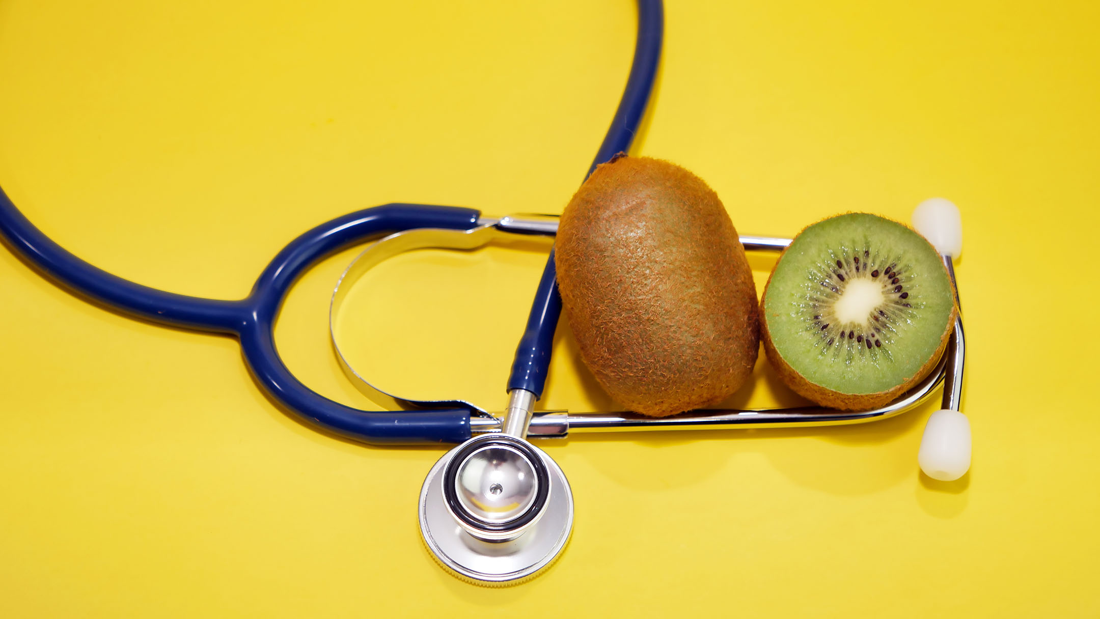 Whole kiwi fruit and halved green kiwifruit encircled within navy blue stethoscope