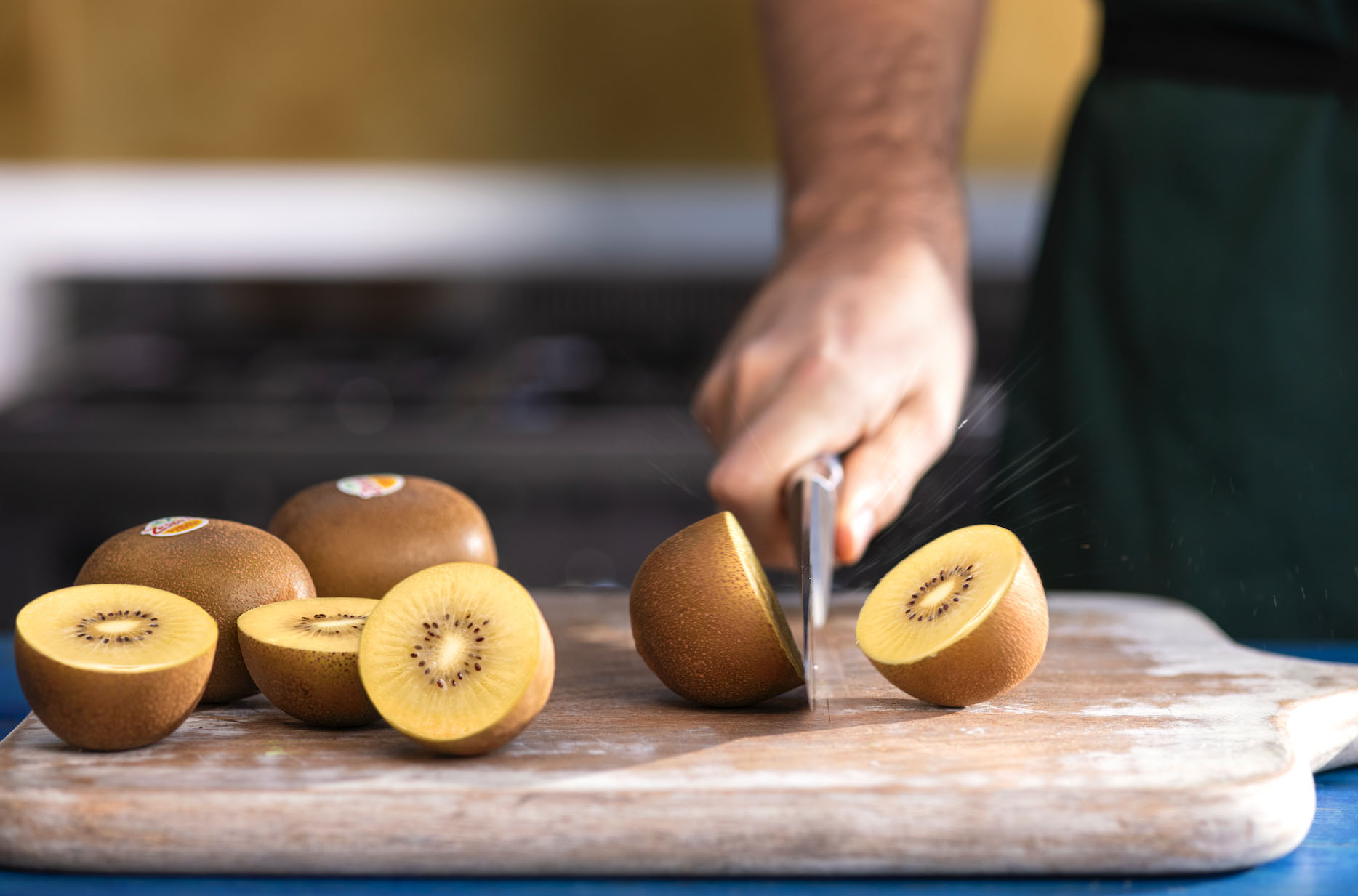 Hand cutting golden kiwi fruit in half along with halved and whole kiwi fruit