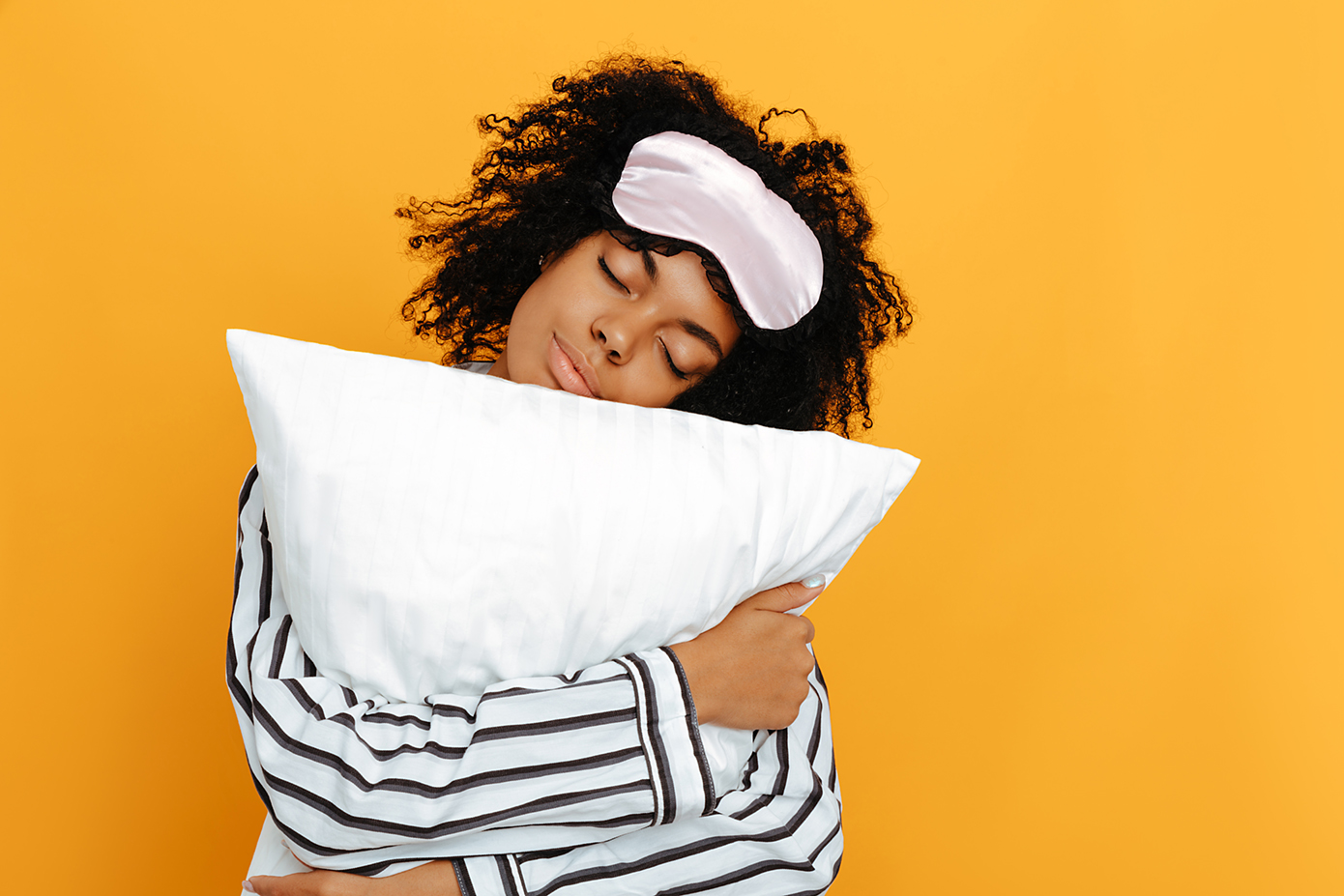 Girl in black and white striped jammies hugging pillow and wearing face mask on forehead