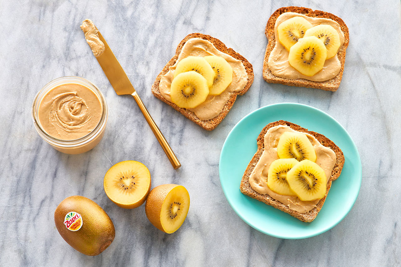 Thick raisin toast with cream cheese and golden kiwifruit drizzled with honey on a white plate