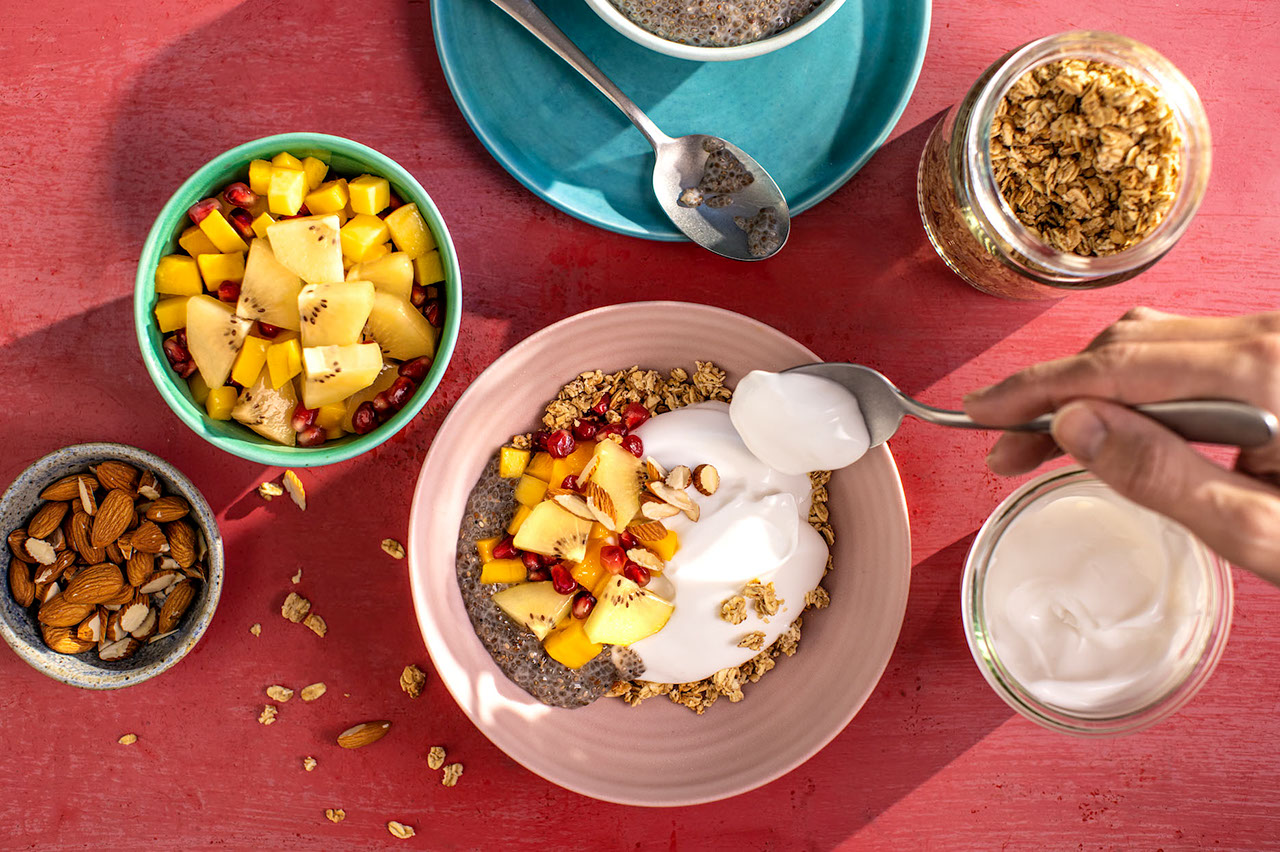 Spoonful of yogurt over bowl of granola with Zespri SunGold Kiwifruit, pomegranate and chia seeds