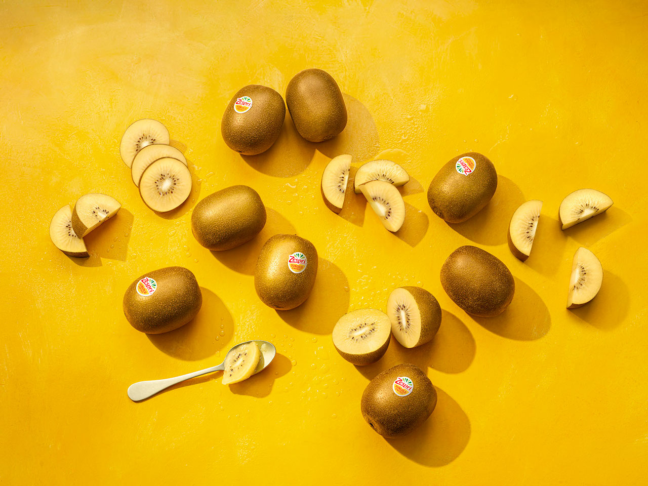 Whole Zespri SunGold kiwifruit and slices of golden kiwifruit on a yellow background