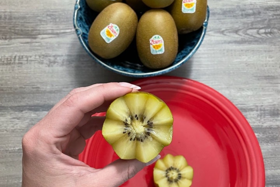 kiwi fruit cut into flower shape, hand holding kiwi flower alongside bowl of whole Zespri SunGold kiwi”