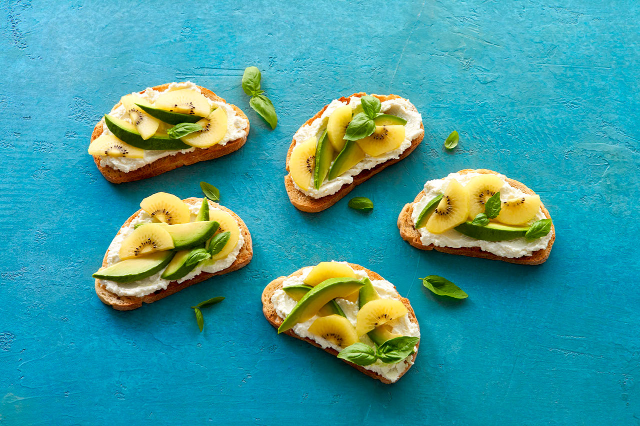 Snack of  golden kiwi fruit and whipped feta cheese on toast with avocado and basil